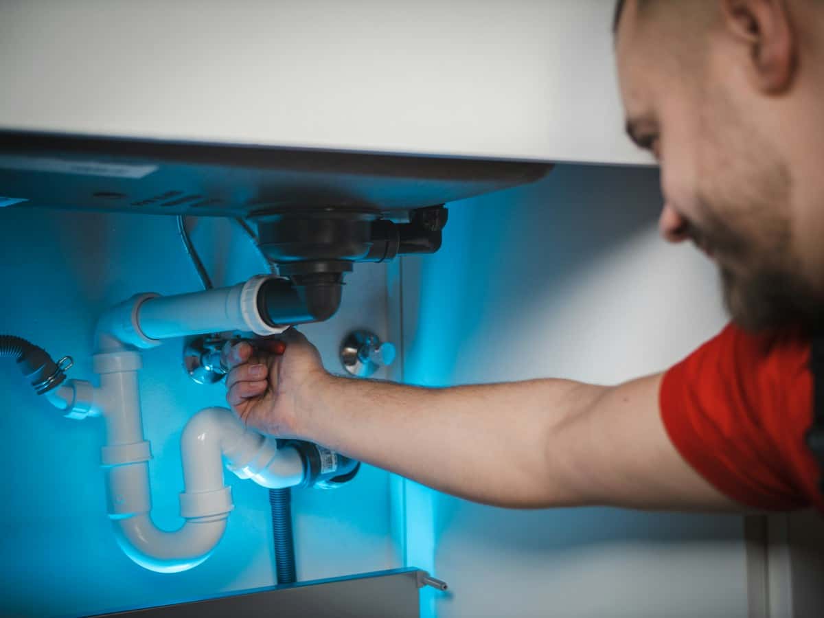A plumber smiling while fixing pipes under a sink
